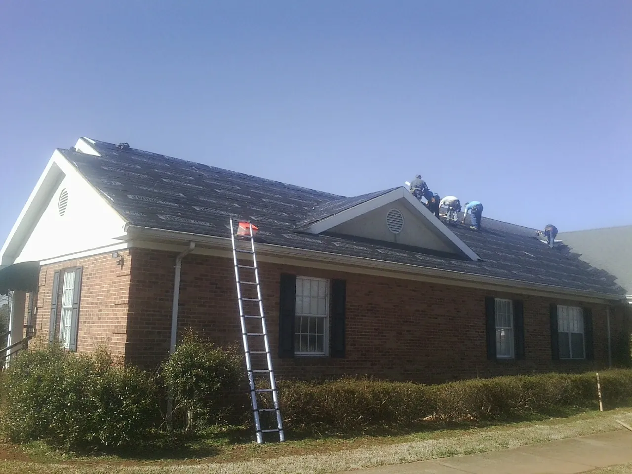Crew tearing shingles off a brick ranch roof with a ladder set — Metal Roof Repair work by our crew in Idyllwild