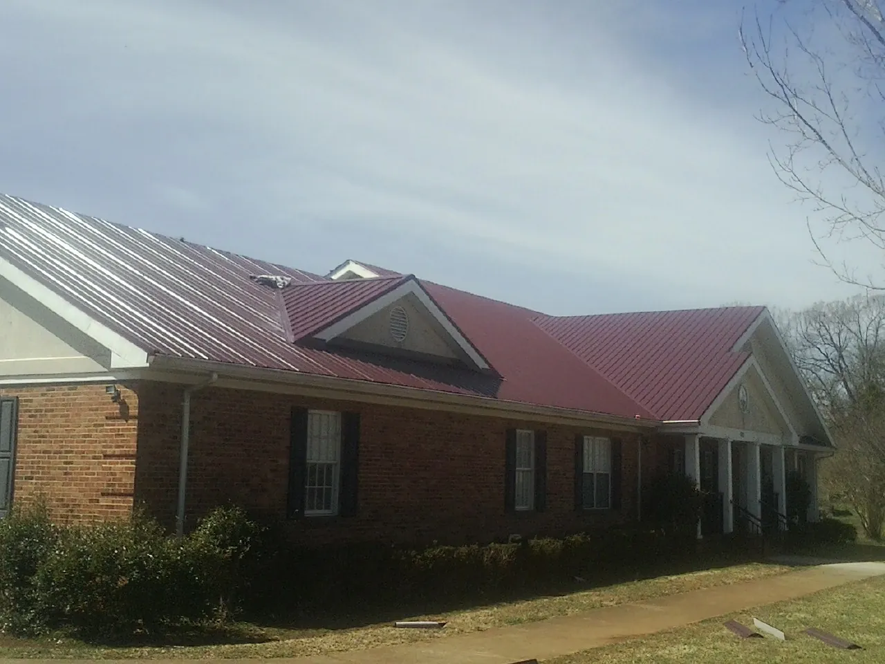 Red metal roof with gabled entries on a long brick building, from a Hail Damage Roof Repair job in Idyllwild