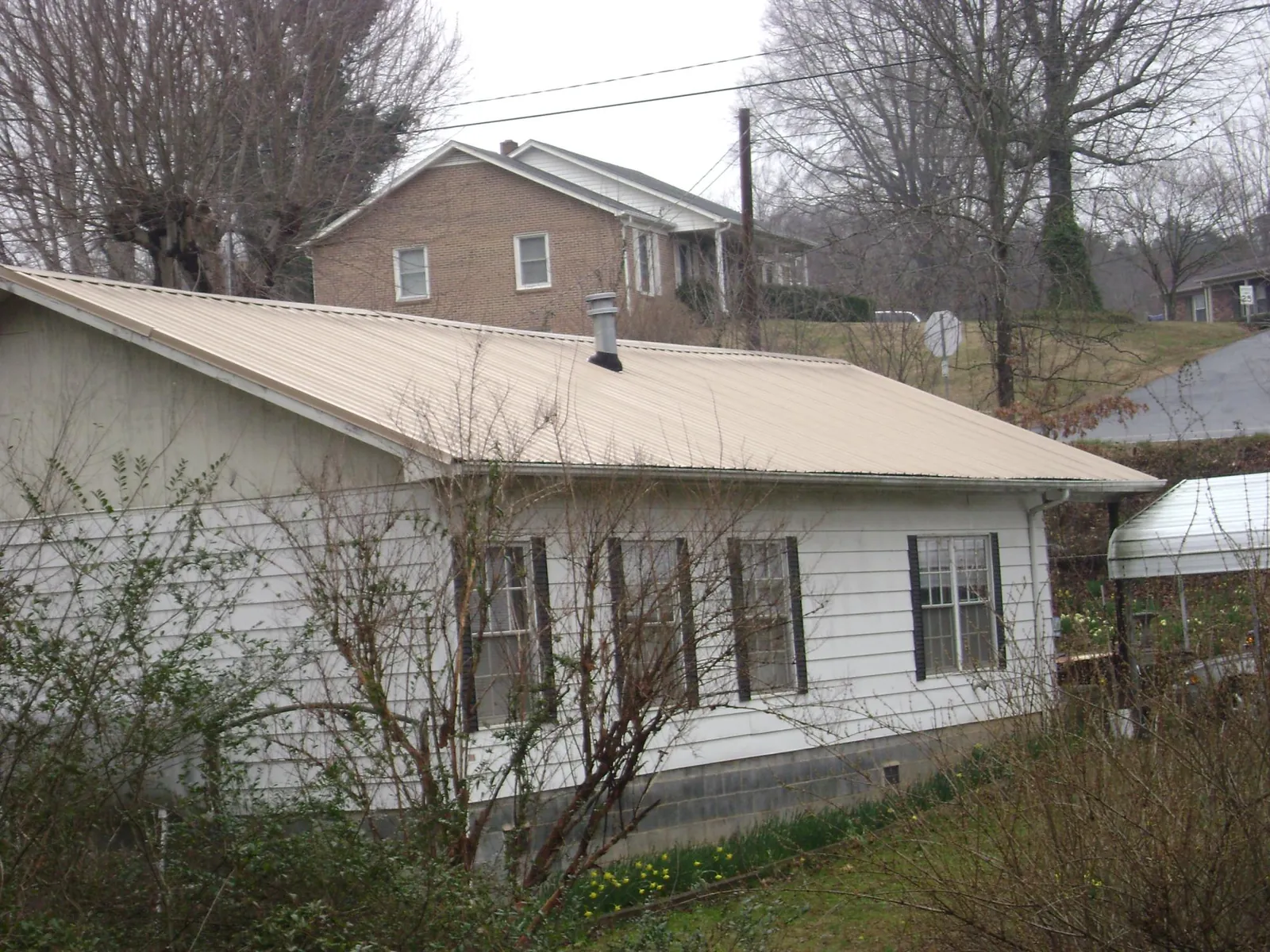Tan metal roof on a white sided house set into a hillside — Commercial Roofing by Roofing Brothers in Idyllwild